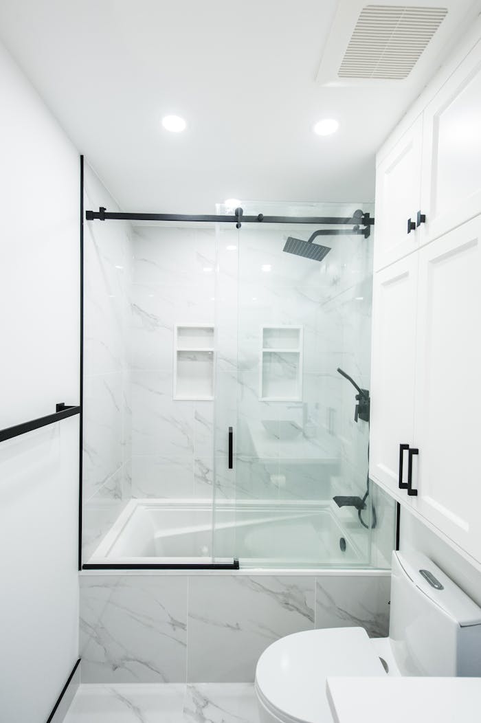 Sleek and modern bathroom featuring white marble tiles, glass shower doors, and black accents.